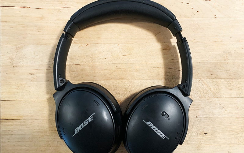 A pair of black Bose Quiet Comfort 45 headphones against a wooden background.