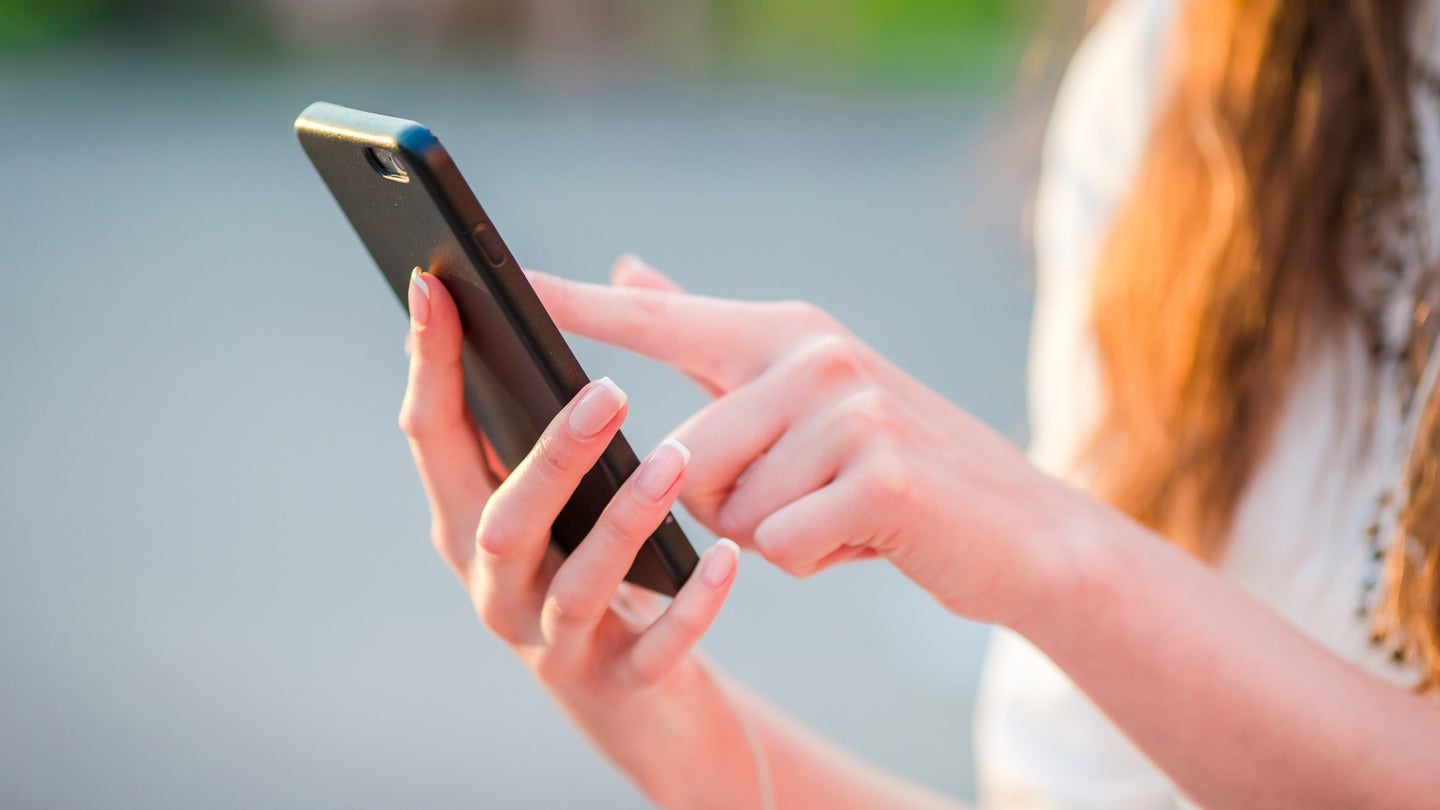 Closeup of female hands is holding cellphone outdoors on the street in evening lights.