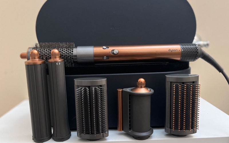 A copper and silver Dyson Airwrap displayed on a white shelf against a yellow wall