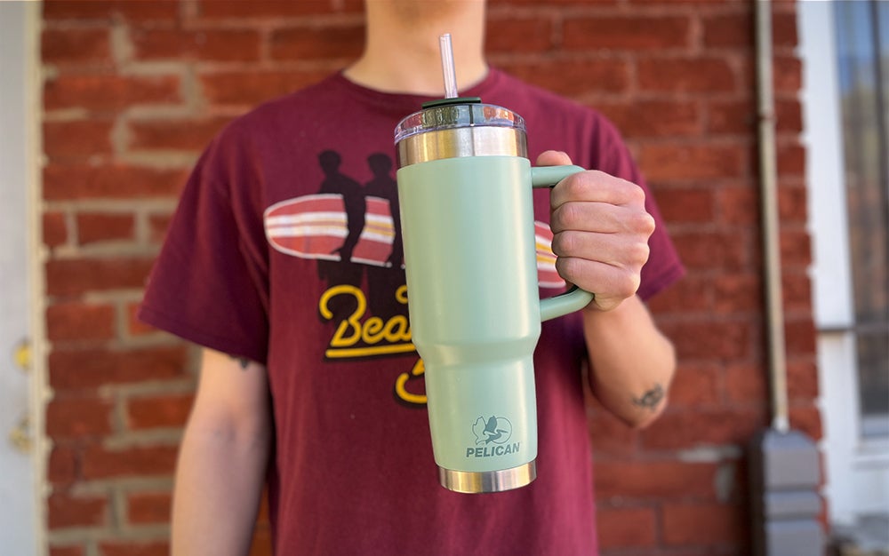 A person standing against a brick wall holding a green Pelican Porter