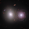 An elliptical galaxy (left) and a spiral galaxy (right). The elliptical galaxy does not have a defined center, and looks like a shining bright light. The spiral galaxy has a defined center with arms swirling around it. The image includes near-infrared light from the James Webb Space Telescope and ultraviolet and visible light from the Hubble Space Telescope.